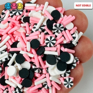 May include: A mix of pink, white, and black polymer clay sprinkles. The sprinkles include small circles, long thin sticks, and larger circles with a black and white striped design. The text "NOT EDIBLE" is visible in the upper right corner of the image.