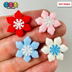 May include: Four snowflake-shaped ornaments in red, pink, blue, and white.  The ornaments are not edible.  "NOT EDIBLE" is printed in black text on a white background in the upper right corner of the image.  The text "PLAYCODES" is printed in black text on a white background in the lower left corner of the image.