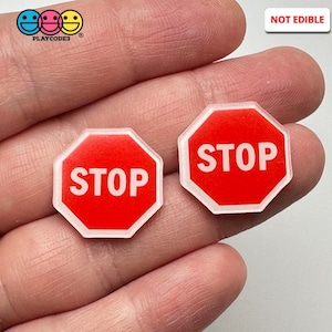 May include: Two red and white stop sign shaped charms. Each charm has the word "STOP" in white letters on a red background. The charms are octagonal and have a clear border. The upper right corner of the image has the text "NOT EDIBLE".