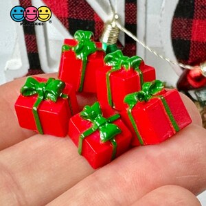 May include: Five miniature red gift boxes with green bows and ribbon. The boxes are arranged in a pile on a hand.
