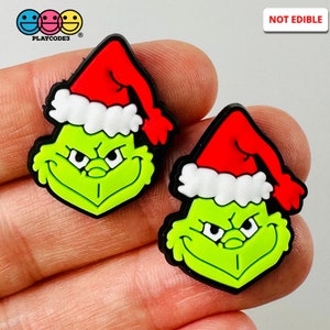 May include: Two green cartoon character shoe charms with red Santa hats and white trim. The charms have black outlines and the text "NOT EDIBLE" is in a white rectangle in the upper right corner.