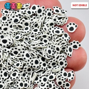 May include: A collection of white and black paw print-shaped polymer clay slices. The slices are small and have a flat back. The image also includes the text "NOT EDIBLE" in a red rectangle and the logo "PLAYCODEZ".