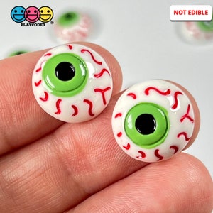 May include: Two green googly eyes with red veins on a white background. The eyes are about 1 inch in diameter. The eyes are not edible. "NOT EDIBLE" is written in black text on a white background.