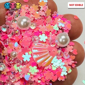 May include: Pink, white, and iridescent glitter mix with a seashell, hearts, and flowers.  The glitter is not edible.  "Playcode3" is written on the image.