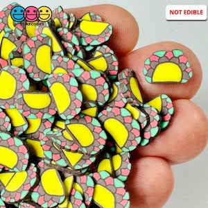 May include: A collection of small, colorful taco-shaped polymer clay slices. Each slice features a yellow filling, surrounded by a brown, pink, and green patterned exterior. The text "NOT EDIBLE" is visible in the upper right corner.