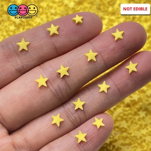 May include: Close-up of yellow star-shaped sprinkles scattered on a surface. The sprinkles are small and have a five-point design. The image also includes the text "NOT EDIBLE" in a white box.