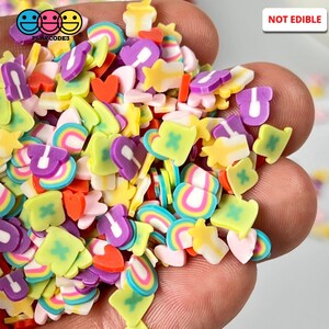 May include: A variety of colorful resin sprinkles in the shape of hearts, rainbows, stars, and other cute designs. The sprinkles are not edible. "NOT EDIBLE" is written in red letters on a white background.