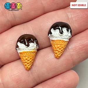 May include: Two miniature ice cream cones with white ice cream, chocolate sauce, and a waffle cone. The cones are not edible and are made of resin.
