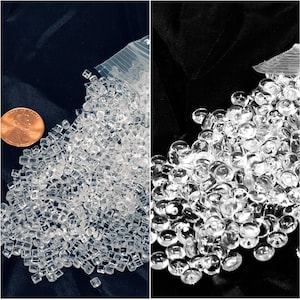 以下が含まれることがあります： 2つの画像が並んでいます。左の画像には、ペニーの隣に、透明で小さな正方形のビーズの山が写っています。右の画像には、透明で丸いビーズの山が写っています。どちらの山も黒い背景にあります。