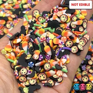 May include: A variety of colorful Halloween-themed sprinkles, including pumpkins, candy corn, and bats. The sprinkles are made of polymer clay and are not edible. "NOT EDIBLE" is written on the image.