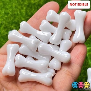 May include: A collection of white plastic bone-shaped beads. The beads are smooth and glossy. NOT EDIBLE.