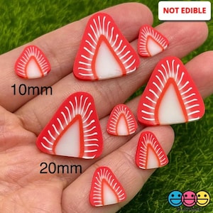 May include: Assortment of seven red and white triangle-shaped strawberry slices in various sizes, ranging from 10mm to 20mm. The slices are made of polymer clay and are not edible. "NOT EDIBLE" is written in white text on a black background in the upper right corner of the image.