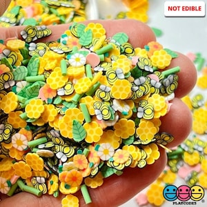 May include: A variety of colorful resin sprinkles for slime, resin, and other crafts. The sprinkles include bees, flowers, honeycomb, and leaves. The text "NOT EDIBLE" is visible in the image.