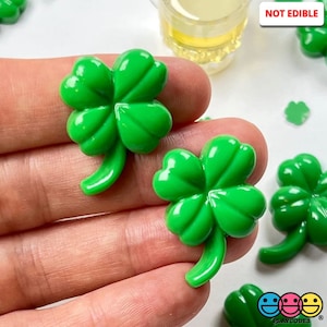 May include: Green plastic shamrock shaped drink charms. The charms are not edible. "NOT EDIBLE" is printed on the image.