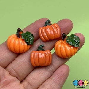May include: Four orange and green pumpkin shaped resin embellishments. The pumpkins have a glossy finish and are perfect for adding a touch of fall to crafts.