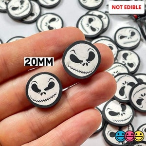 May include: A close-up of a hand holding a variety of black and white 20mm round resin cabochons with a Jack Skellington face design. The text "NOT EDIBLE" is visible in the background.