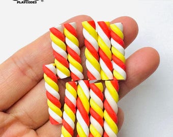 May include: A collection of 12 miniature candy canes, each with a red and yellow swirl pattern. The candy canes are made of polymer clay and are not edible.  NOT EDIBLE.