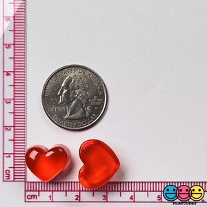 May include: Two red heart-shaped glass beads next to a US quarter. The beads are approximately 1 cm in diameter.