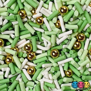 May include: Close-up of a mix of green, white, and gold sprinkles. The sprinkles include small green and white cylinders and gold metallic ball-shaped sprinkles. The image is a close-up shot of the sprinkles.