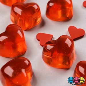 May include: A group of red heart-shaped jelly candies on a white surface. The candies are clear and have a shiny finish.