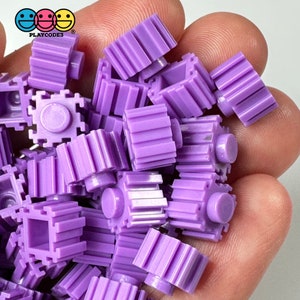 May include: A large pile of purple plastic building blocks with a textured surface. The blocks are in the shape of cubes with a small round stud on top.