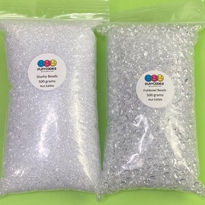 以下が含まれることがあります： 透明なビーズが入った2つの透明なビニール袋。1つは「Slushy Beads」、もう1つは「Fishbowl Beads」と表示されています。各バッグには500グラムのビーズが入っており、「食べられません」と表示されています。