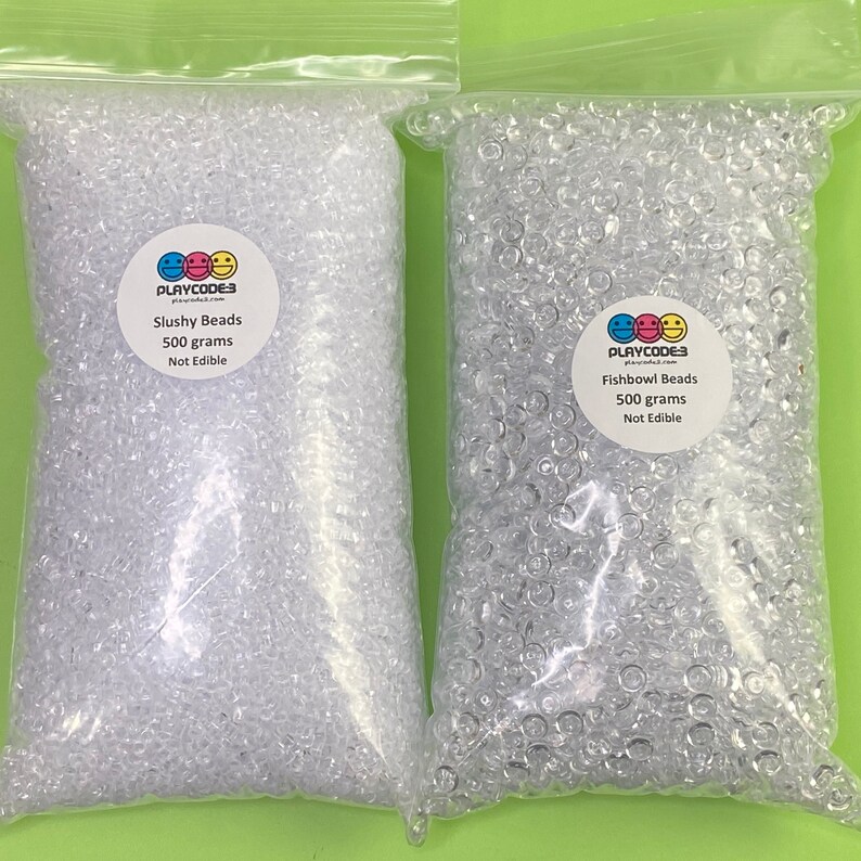 以下が含まれることがあります： 透明なビーズが入った2つの透明なビニール袋。1つは「Slushy Beads」、もう1つは「Fishbowl Beads」と表示されています。各バッグには500グラムのビーズが入っており、「食べられません」と表示されています。