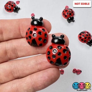 May include: A set of red and black ladybug figurines with black dots. The ladybugs are made of plastic and are not edible. The text "NOT EDIBLE" is visible in the image.