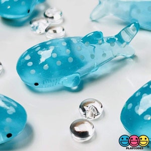 May include: A set of four blue and white whale shark figurines with white polka dots. The figurines are made of clear plastic and have a glossy finish.