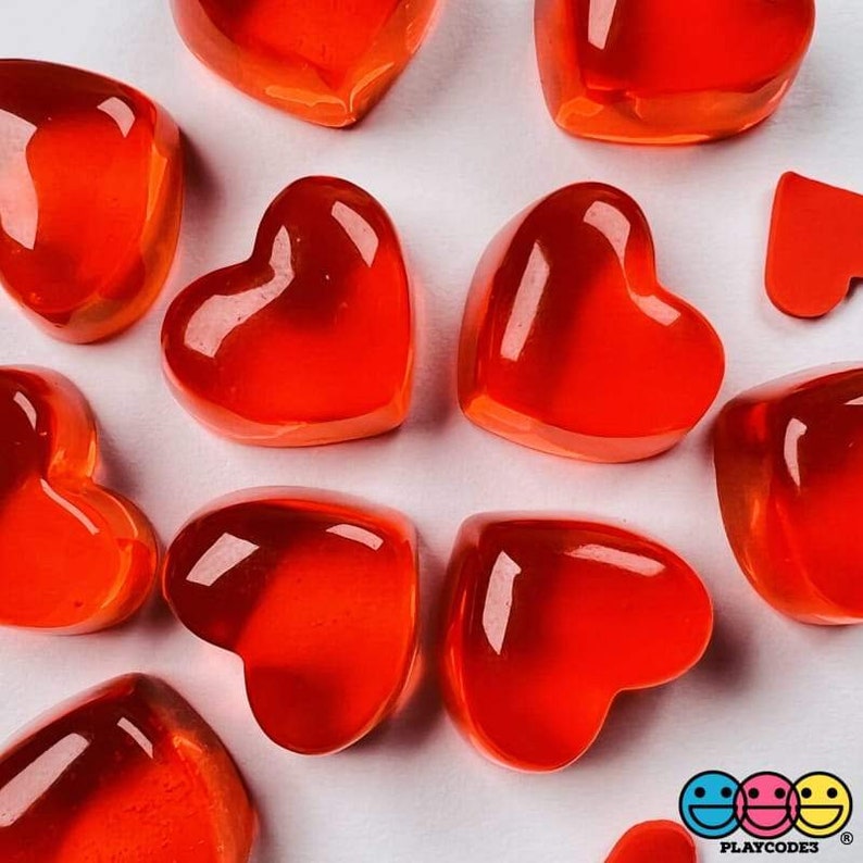 May include: A collection of red heart-shaped jelly candies on a white surface. The candies are translucent and have a glossy finish.