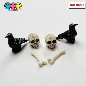 May include: A collection of Halloween-themed miniature decorations. The set includes two black raven figurines, two off-white skull figures, and two bone-shaped figures. The phrase "NOT EDIBLE" is displayed in a white rectangle.