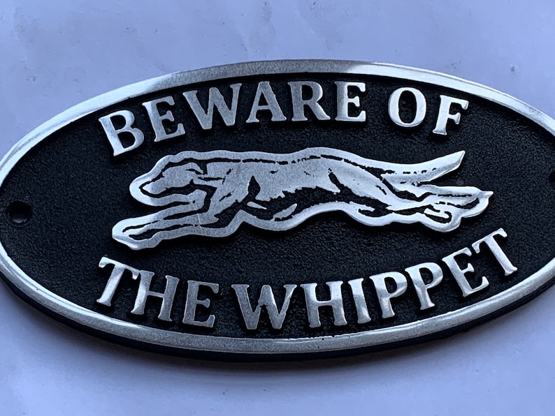 May include: A black and silver oval sign with the text "Beware of the Whippet" and a silver silhouette of a whippet running.