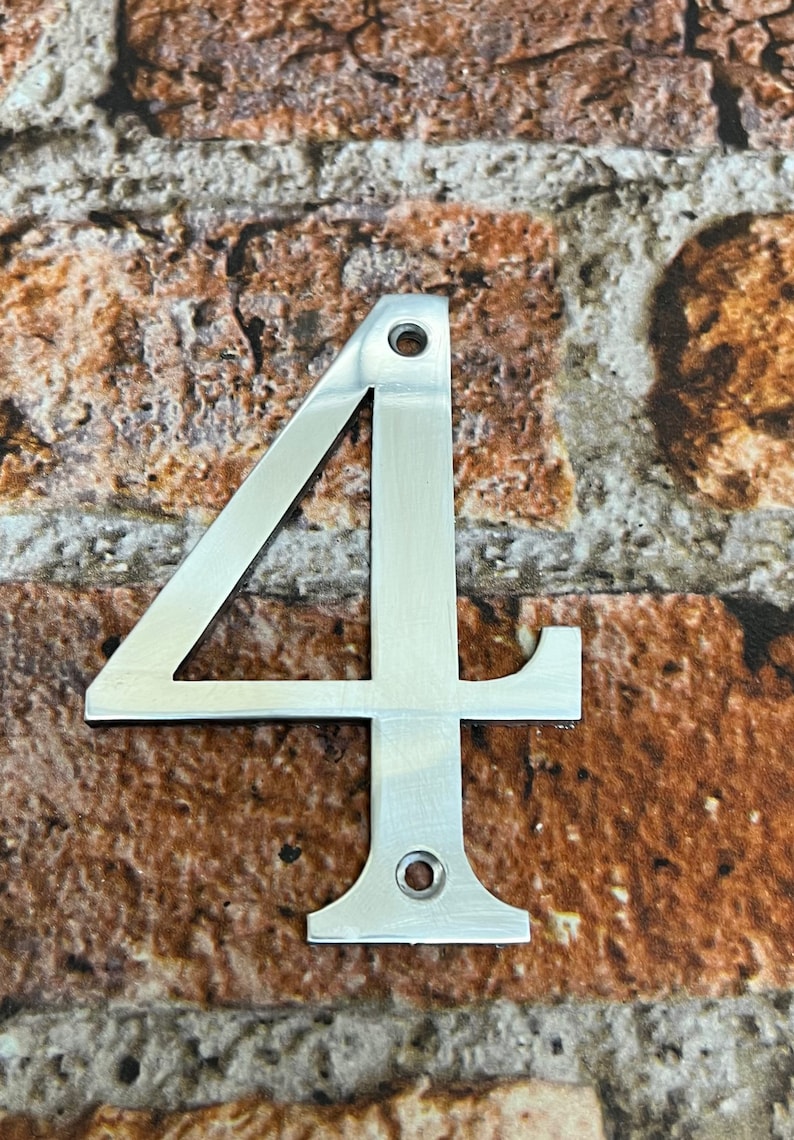 K&ouml;nnte beinhalten: Eine silberne Hausnummer vier aus Metall. Die Nummer ist an einer Backsteinwand befestigt.