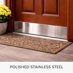 May include: A polished stainless steel door threshold is installed at the base of a wooden door. A rectangular brown patterned rug sits in front of the door. A potted plant with yellow flowers is to the left.