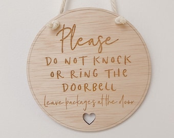 May include: A round wooden sign with the text "Please do not knock or ring the doorbell. Leave packages at the door." The sign has a small heart cutout in the bottom.