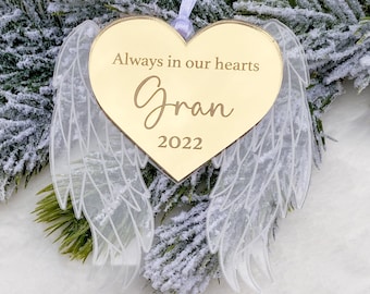 May include: Gold heart-shaped bauble with white angel wings. The bauble has the text "Always in our hearts Gran 2022" engraved on it.