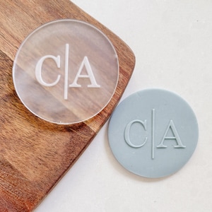 May include: Two round, clear and blue, custom monogrammed cookie cutters. The cutters are engraved with the initials "C|A".