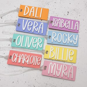 May include: Eight colourful luggage tags with names printed in white. The names are Dali, Vera, Isabella, Rocky, Billie, Charlotte, Myra, and Oliver.