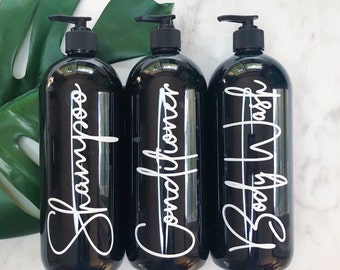 May include: Three black pump bottles with white script labels. The labels read "Shampoo", "Conditioner", and "Body Wash".