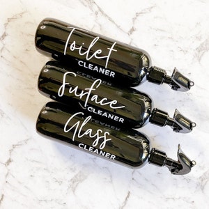 May include: Three black spray bottles with white labels. The labels read "Toilet Cleaner", "Surface Cleaner", and "Glass Cleaner".