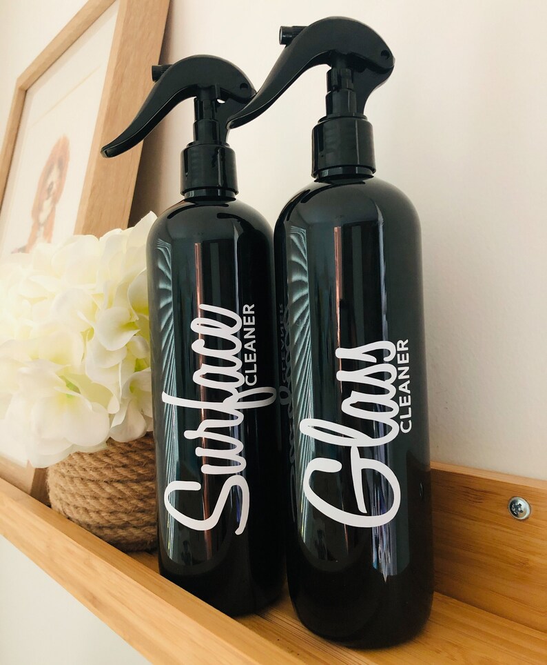 May include: Two black spray bottles with white labels. The bottle on the left says "Surface Cleaner" and the bottle on the right says "Glass Cleaner".