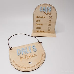 May include: Two wooden signs. One is a cafe menu with "Cafe Menu" in light blue letters, and a list of items. The other sign says "Dali's Kitchen" in light blue letters, with a heart cutout and text around the edge.