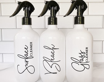 May include: Three white spray bottles with black trigger sprayers and black labels. The labels read "Surface Cleaner", "Bleach", and "Glass Cleaner".