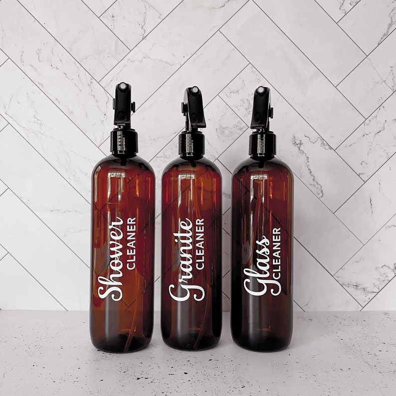 May include: Three amber glass spray bottles with black spray tops and white labels. The labels read "Shower Cleaner", "Granite Cleaner", and "Glass Cleaner".