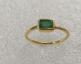 May include: A gold ring with a square emerald green gemstone set in a gold bezel.