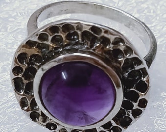 May include: A silver ring with a textured band and a large, round, purple amethyst gemstone.