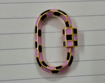 May include: A pink and black enamel oval-shaped clasp with a gold finish. The clasp is made of a series of interlocking squares.