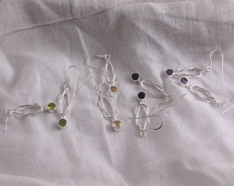 Könnte beinhalten: Ein Set aus fünf silbernen Ohrringen mit verschiedenen Edelsteinen. Die Ohrringe haben ein verdrehtes Knotendesign und sind in Grün, Gelb, Lila und Schwarz erhältlich.
