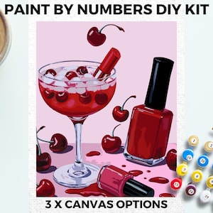 Puede incluir: Kit de pintura por números DIY con una copa de cóctel llena de cerezas rojas y un pintalabios rojo, junto con dos botellas de esmalte de uñas rojo. El fondo es rosa. 3 opciones de lienzo.