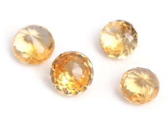 May include: Four faceted, round gemstones in shades of yellow and gold are arranged on a white background. The gems have a brilliant cut, reflecting light and showcasing their clarity. The gemstones are likely citrine or a similar type of crystal.